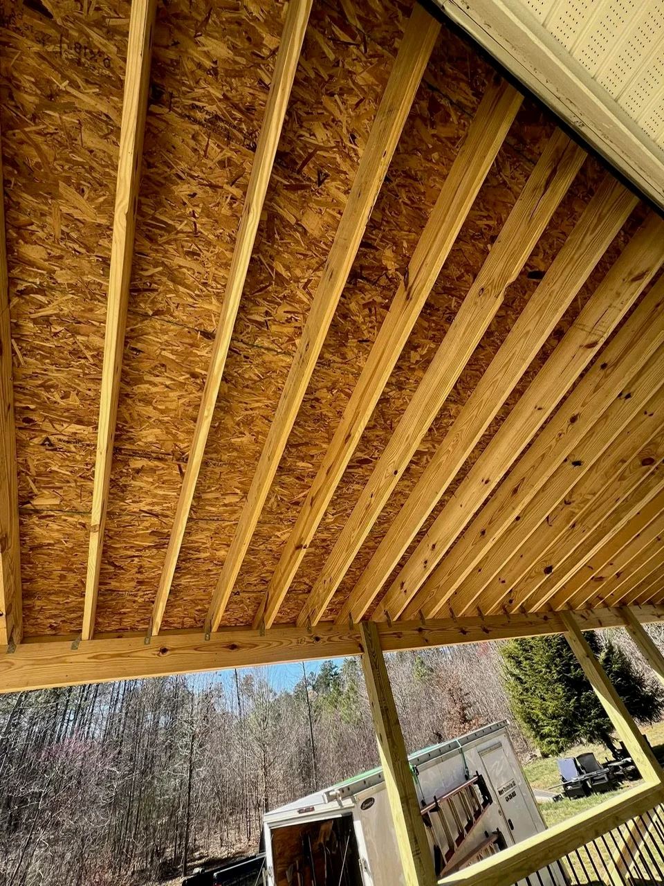 Wooden patio framing with exposed beams, OSB sheathing, and angled rafters under construction