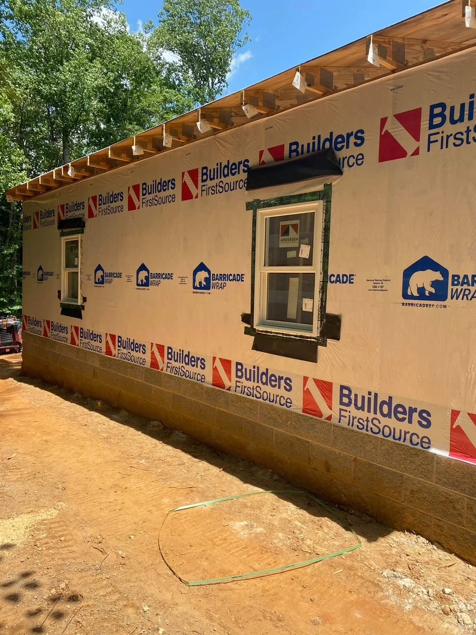 House wrap weather barrier installation on new construction framing with exposed trusses and prepared openings