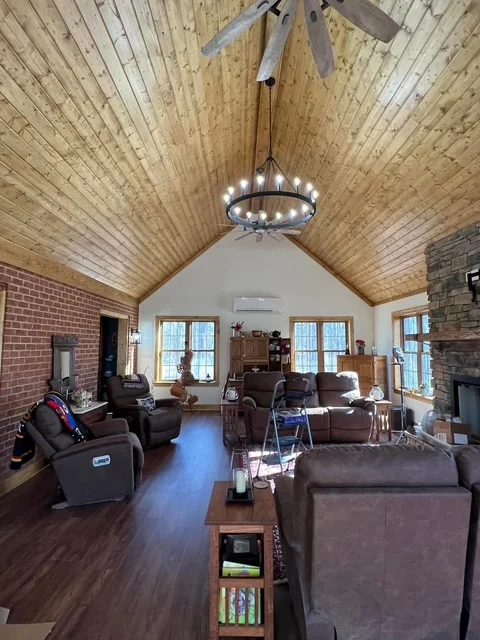 Vaulted wood ceiling with beam, hardwood floors, brick walls, and integrated pendant lighting in great room