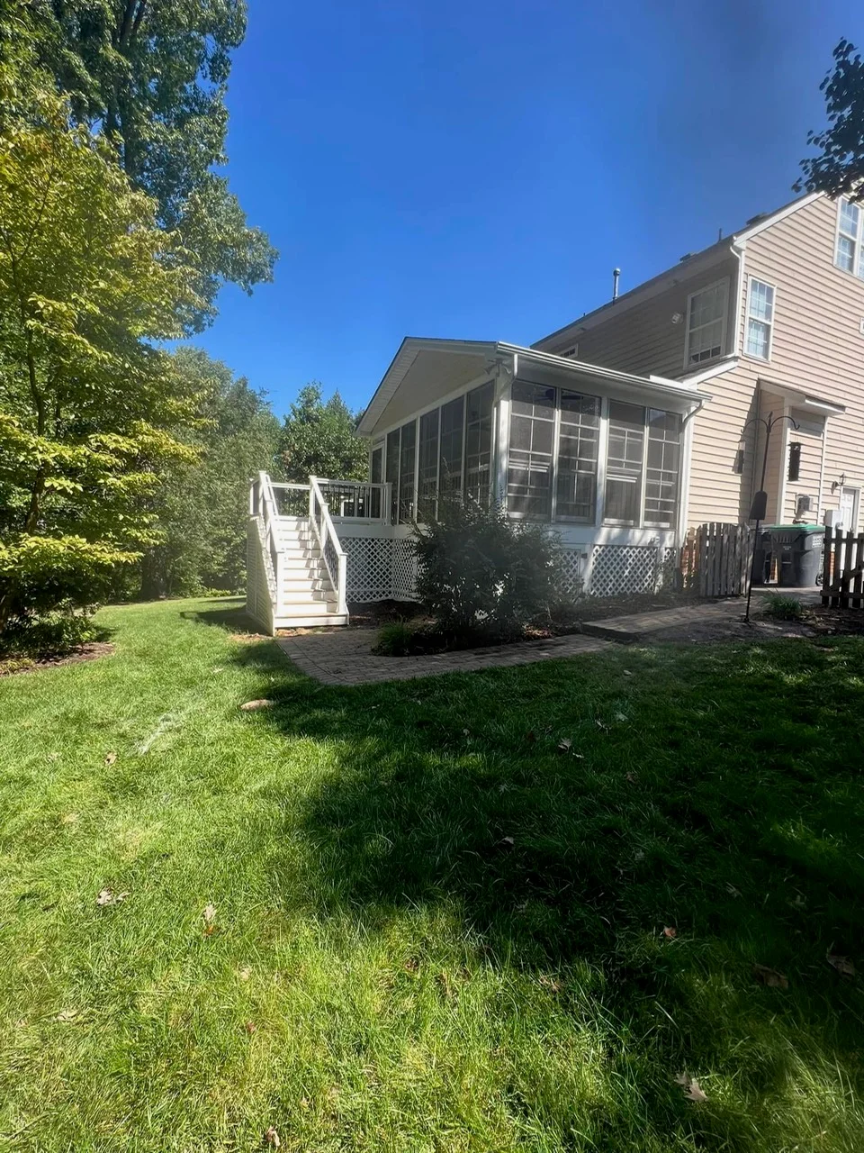White screened porch addition with large windows, lattice skirting, and deck stairs on residential home
