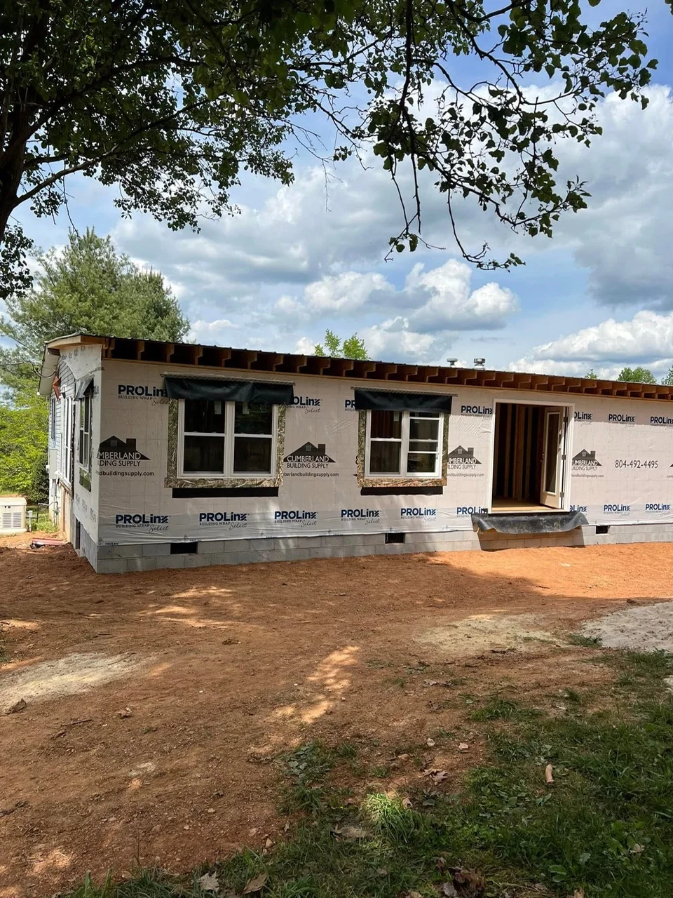 Mobile home exterior with new windows, house wrap, and foundation work in progress