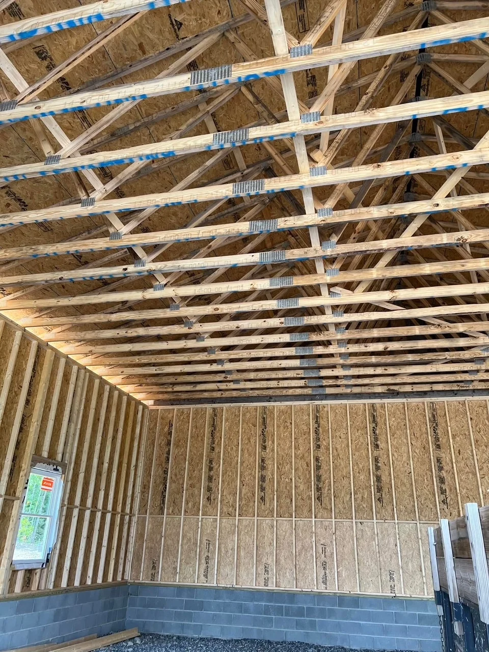 Engineered roof trusses with blue barriers, lumber framing, and OSB wall sheathing in residential construction