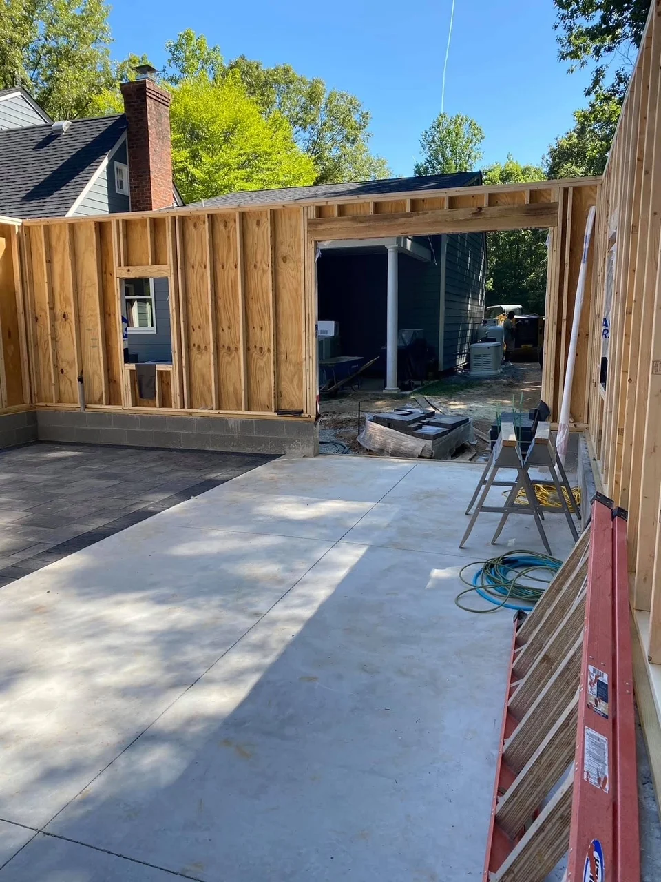 Wood-framed residential addition with cedar siding, concrete patio, and open beam structure under construction
