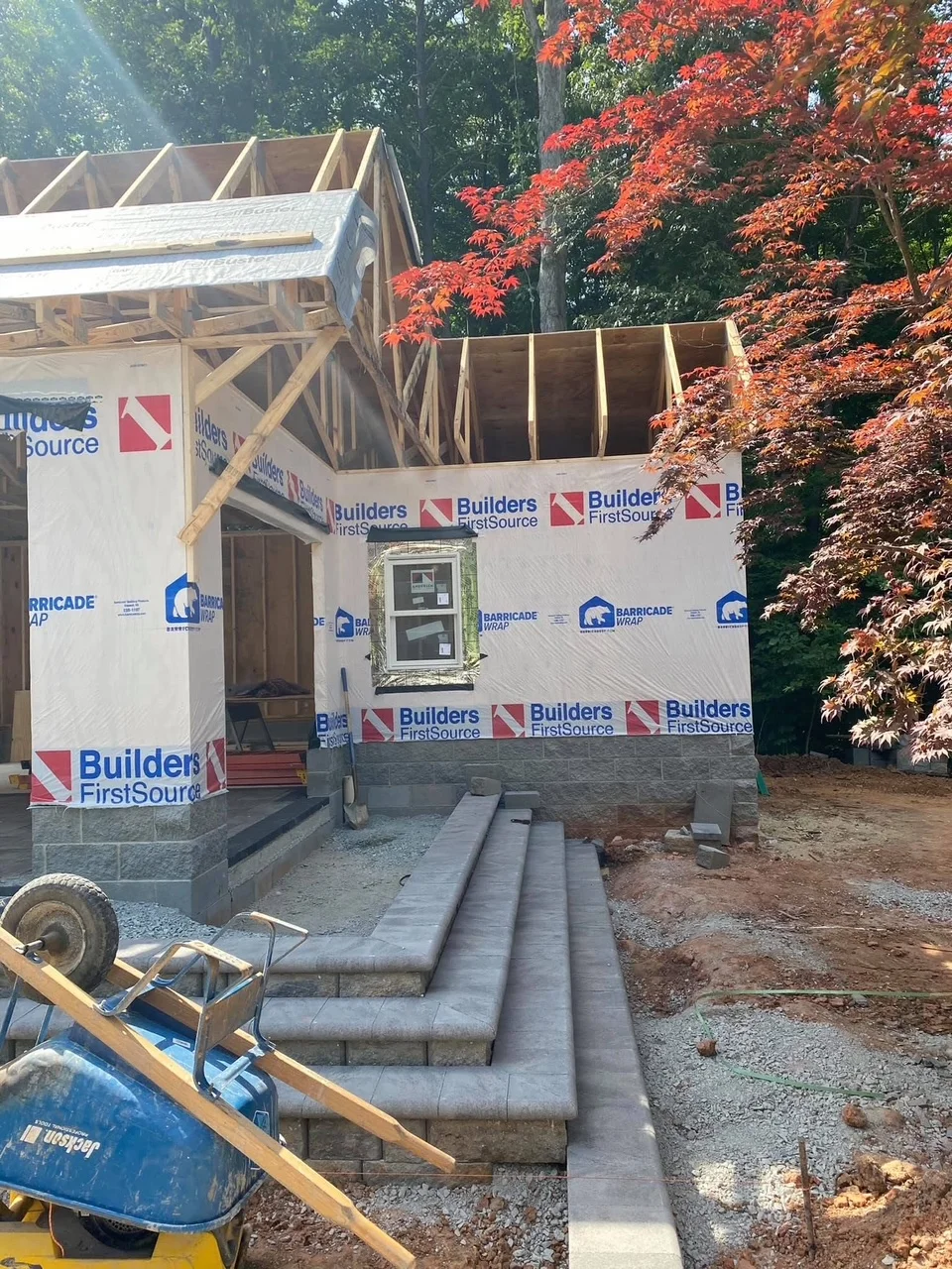 Wood-framed house under construction with concrete foundation, stone veneer, and roof trusses