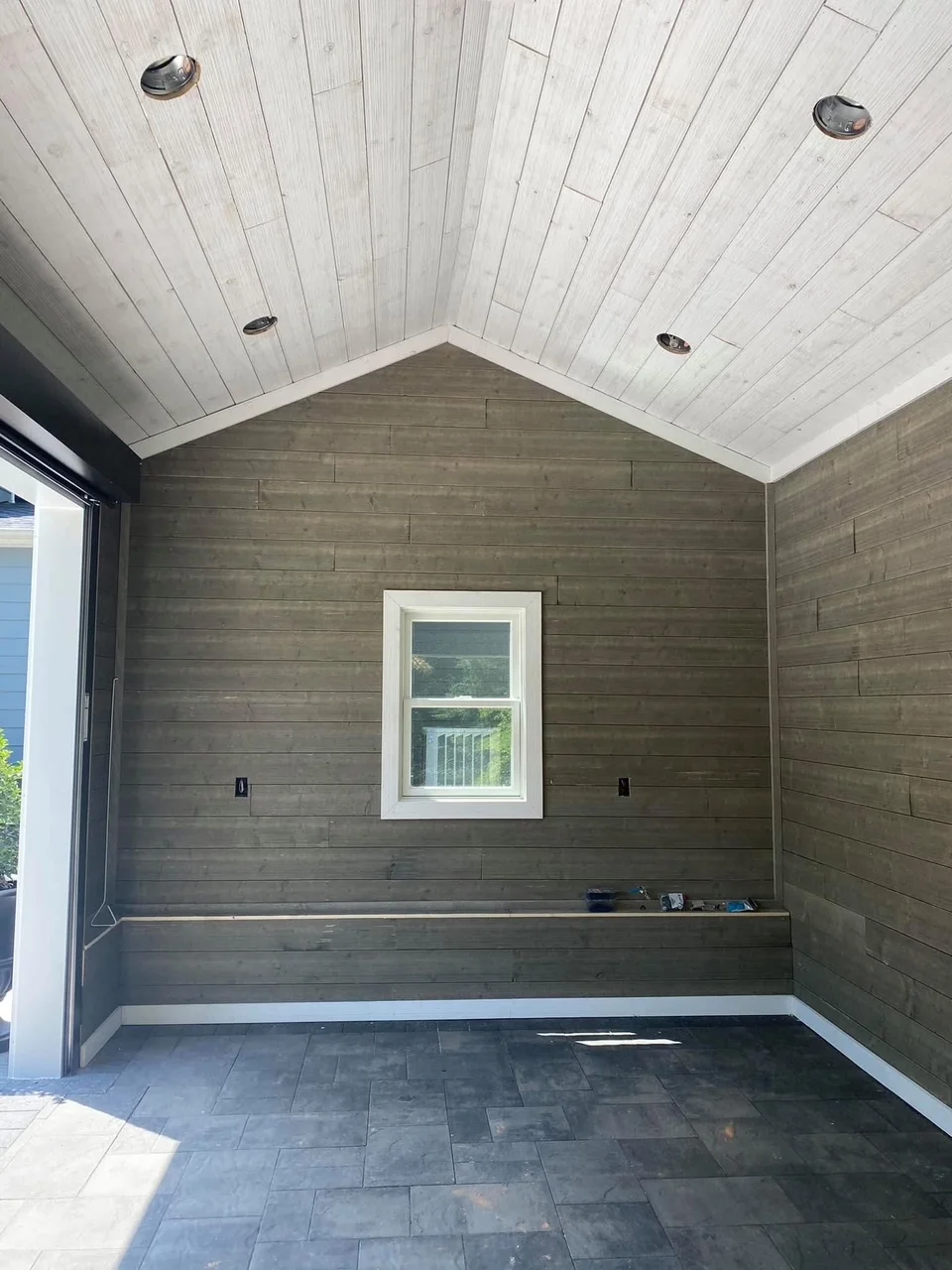 Garage interior with white shiplap ceiling, dark wood plank walls, slate tile floor, and centered window