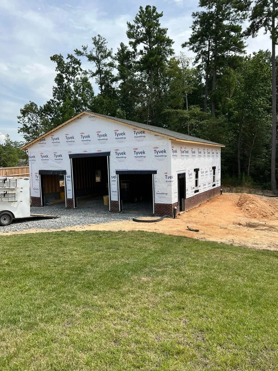 New garage construction with brick foundation and Tyvek wrap, multiple garage door openings
