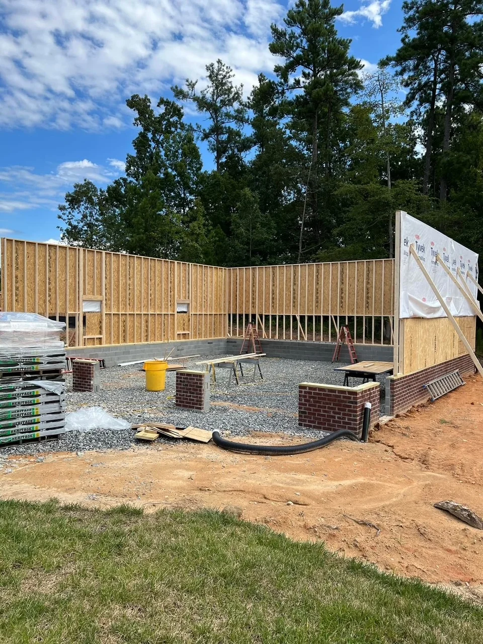 Residential home framing with wood studs, OSB sheathing, concrete foundation, and brick stem walls under construction