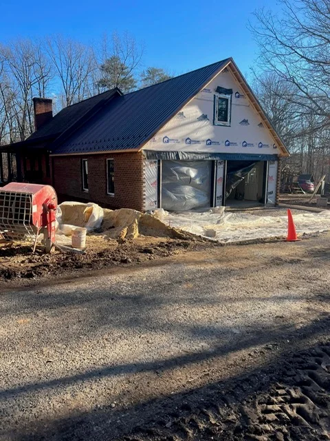 Brick residential addition with dark metal roof and garage doors under construction