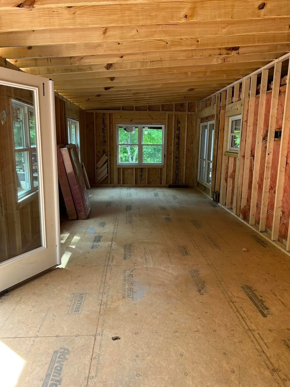 Sunroom interior framing with wood beams, studs, windows, and OSB subfloor
