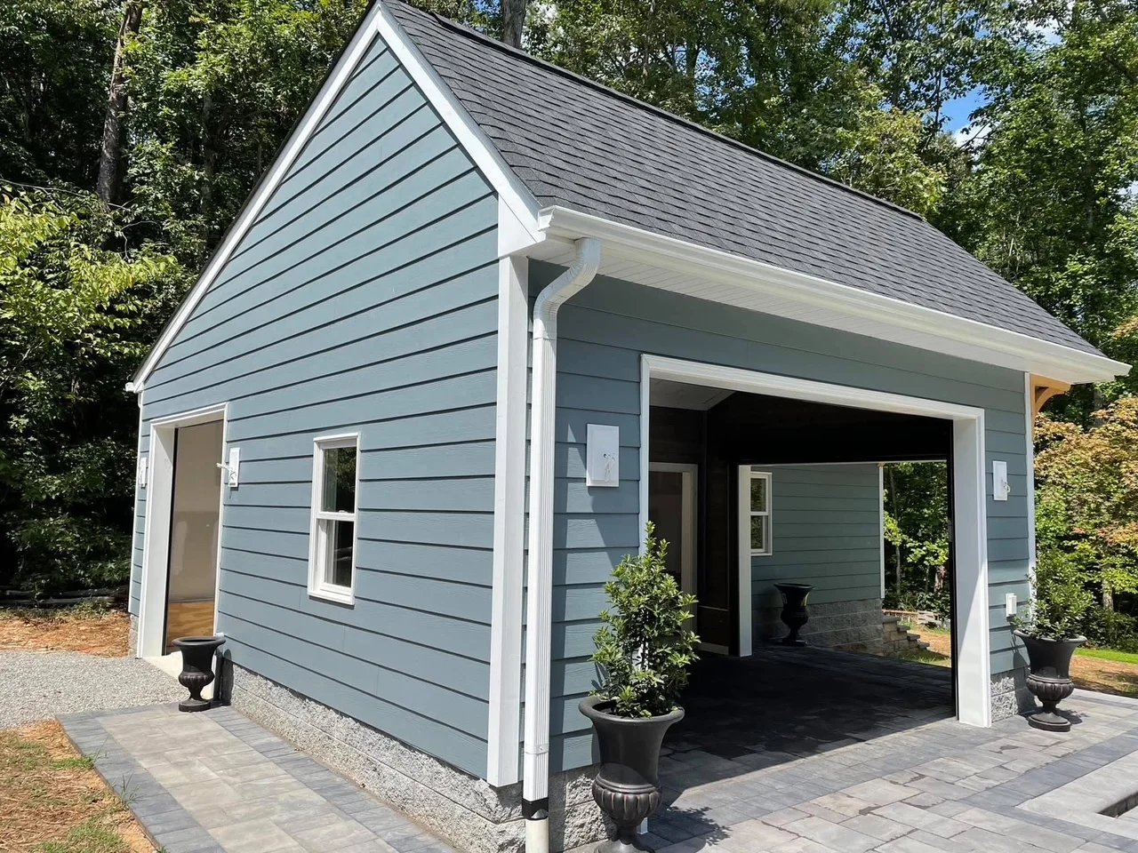 Slate blue carport with white trim, shingle roof, and paver foundation